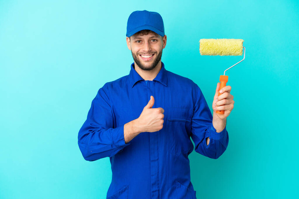 Painter caucasian man isolated on blue background giving a thumbs up gesture - Фото, изображение
