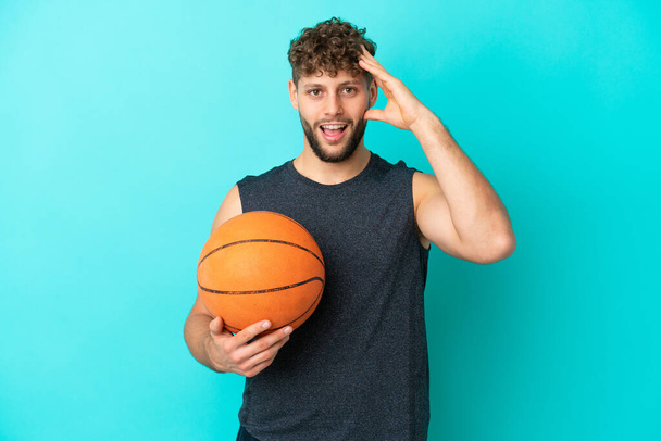 Schöner junger Mann spielt Basketball isoliert auf blauem Hintergrund mit überraschendem Gesichtsausdruck - Foto, Bild