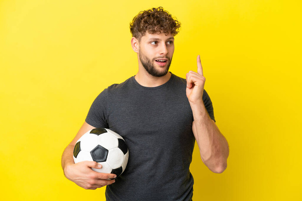 przystojny młody piłkarz człowiek odizolowany na żółtym tle myśląc pomysł wskazując palcem w górę - Zdjęcie, obraz