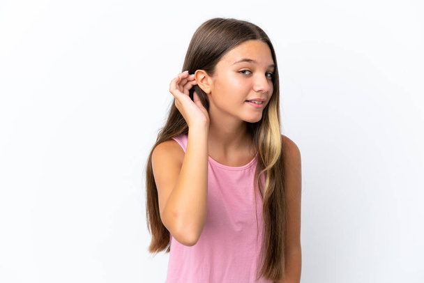 Kleines kaukasisches Mädchen isoliert auf weißem Hintergrund, hört etwas, indem es die Hand ans Ohr legt - Foto, Bild