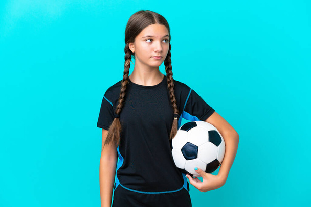 Pequeña chica caucásica aislada sobre fondo azul con pelota de fútbol - Foto, Imagen