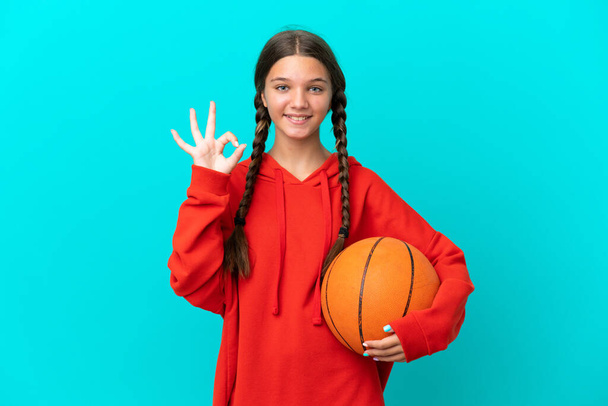 Маленькая кавказская девочка, играющая в баскетбол на голубом фоне. - Фото, изображение