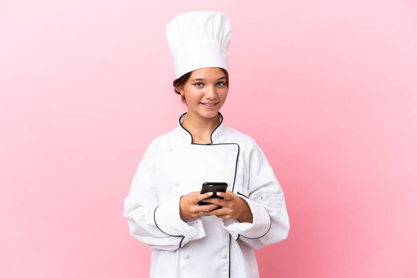 Pequeña chica chef caucásica aislada sobre fondo rosa enviando un mensaje con el móvil - Foto, Imagen