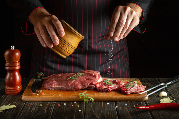 Професійний шеф-кухар солі сирої свіжої яловичини перед обсмажуванням або смаженням. Робоче середовище на кухні ресторану або готелю
 - Фото, зображення