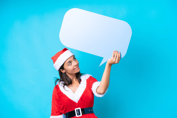 Young hispanic woman dressed as mama noel isolated on blue background holding an empty speech bubble - Foto, imagen