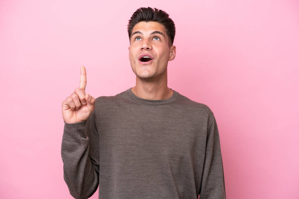 Young caucasian man isolated on pink background pointing up and surprised - Photo, Image
