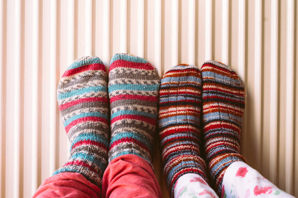 Familie in warme gebreide wollen sokken in de buurt van huis verwarming in de koude wintertijd. Verwarmingsseizoen concept. Energiecrisis Europa. Toenemende prijs van aardgas voor huisverwarming. Overgang naar hernieuwbare energiebronnen - Foto, afbeelding