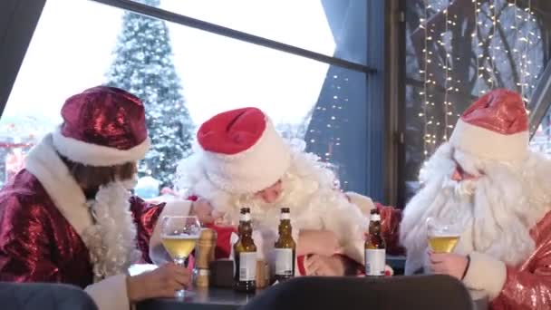 Dronken mannen in kerstmankostuums die rusten in een pub. De kerstman viel in slaap aan tafel. Kersttijd. Kerstman groep - Video