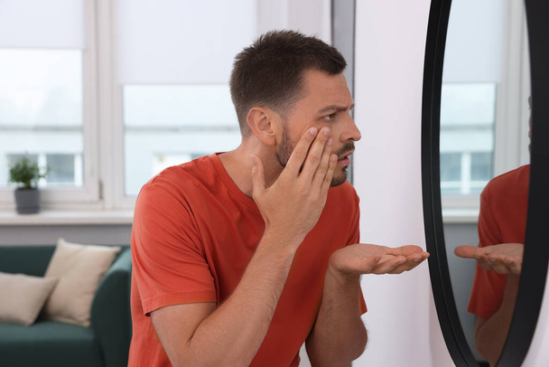Sleep deprived man looking at himself in mirror indoors - Foto, Imagen