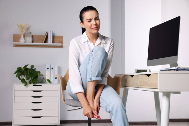 Mujer joven frotando el pie dolorido en la oficina - Foto, imagen