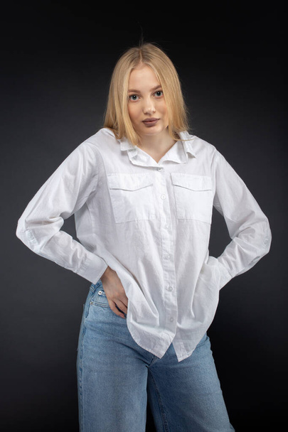 Блондинка в джинсах и белой рубашке на черном фоне - Фото, изображение