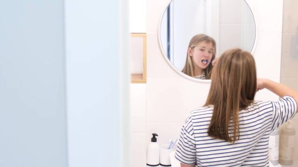 Teini-ikäinen tyttö harjaa hampaansa huolellisesti kylpyhuoneen peilin edessä. Lasten hammashygienia - Valokuva, kuva