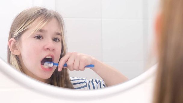 Egy tinédzser lány óvatosan mossa a fogát a fürdőszoba tükör előtt. Gyermekek fogászati higiéniája - Fotó, kép