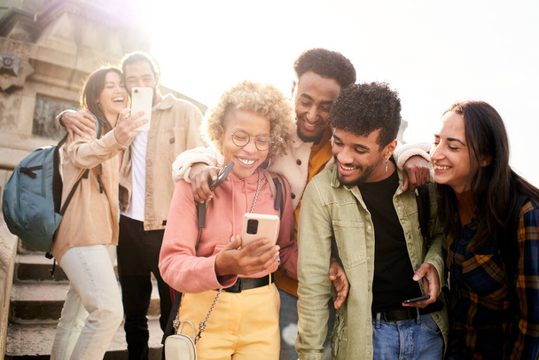 Quatro amigos alegres assistindo smartphone ao ar livre. Pessoas usando dispositivos digitais e compartilhando em redes sociais juntas. Foto de alta qualidade - Foto, Imagem