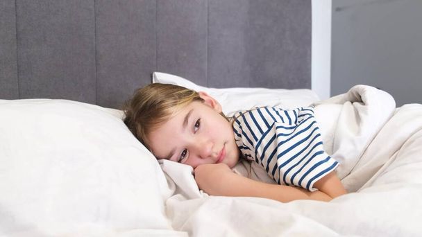 Una linda adolescente está acostada en una cama grande con ropa de cama blanca. Buenos días. Un dormitorio con un interior moderno - Foto, imagen