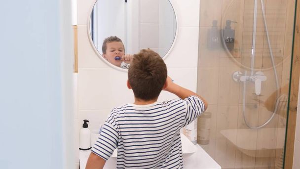 A kis aranyos fiú fogat mos a tükör előtt a fürdőszobában, modern belsővel. Gyermekek szájhigiéniája - Fotó, kép