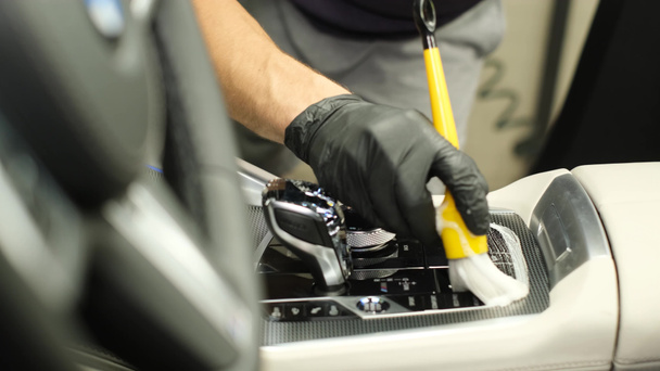 Reinigung des Getriebes eines Neuwagens. Professionelle Reinigung des Fahrzeuginnenraums mit einer Bürste. Eine Männerhand reinigt den Innenraum eines Autos - Foto, Bild