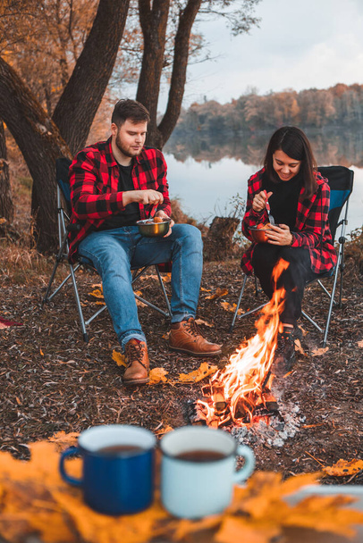 hymyilevä onnellinen pari lepää lähellä tulta ruoanlaitto syksyllä camping käsite - Valokuva, kuva