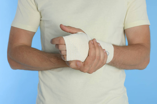 Man with hand wrapped in medical bandage on light blue background, closeup - Foto, immagini