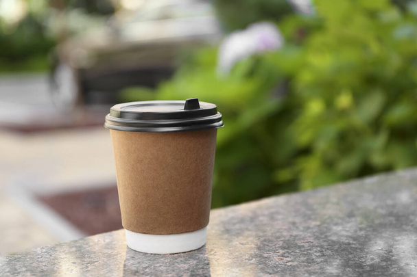 Paper cup with hot coffee on table outdoors, space for text. Takeaway drink - Valokuva, kuva