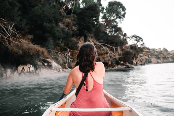 young caucasian woman from the back sitting in a kayak paddling about to reach the trees on the lake shore, tarawera lake, new zealand - Lifestyle travel concept - Fotoğraf, Görsel