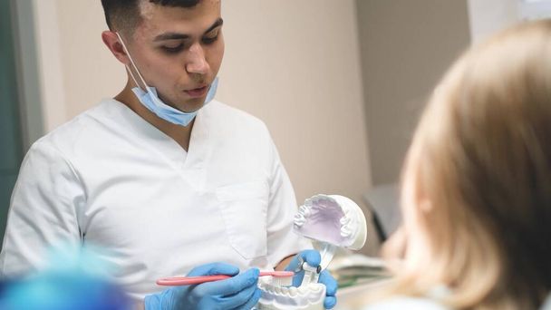 Gyermekfogorvosi konzultáció. Egy fogorvos megmutatja egy próbababán, hogyan kell helyesen fogat mosni. Fogászati betegségek megelőzése tinédzsereknél. - Fotó, kép