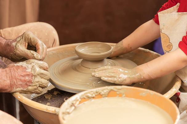 陶芸家と少女の手の水平方向の眺めを閉じ、陶芸家は少女に粘土のカップをモデル化するように教えています。伝統的取引の見習い - 写真・画像