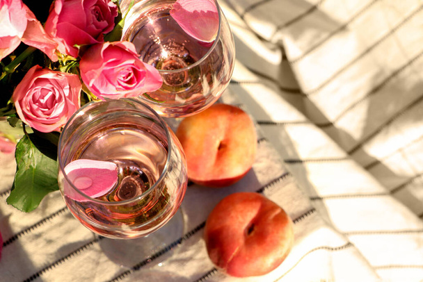 Glasses of delicious rose wine with petals, flowers and peaches on white picnic blanket outside, above view. Space for text - Fotografie, Obrázek