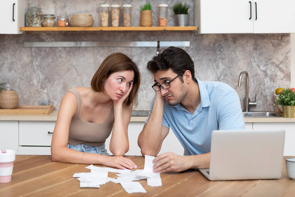 Perheen talouskriisin käsite. Järkyttynyt ja stressaantunut pari, joka laskee kuluja, veroja ja velkoja. Kannettava tietokone ja monet laskut pöydällä - Valokuva, kuva