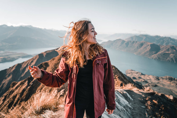 young caucasian woman with long blonde hair holding her head looking to the side smiling at camera happy and content from the mountain in the middle of nature in a calm and quiet place, roys peak, new - Photo, Image