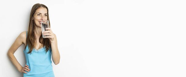 Smiling young woman drinking water from a glass on white background. Banner. - Foto, Imagem