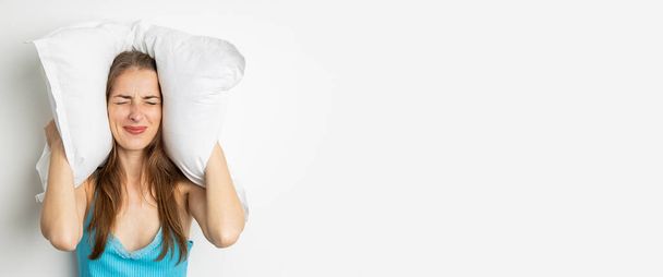 Fermée les yeux, une jeune femme se couvre les oreilles avec un oreiller. Bannière. - Photo, image
