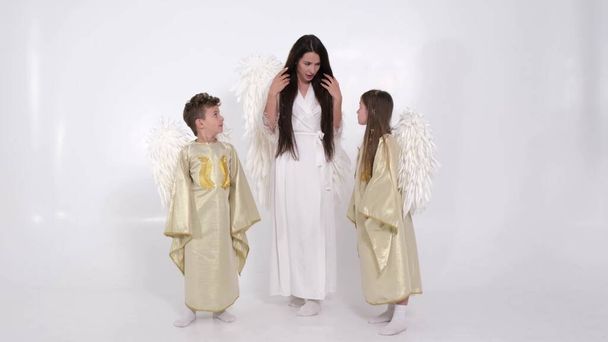 Мама з дітьми дочка і син одягнені в костюми ангела, вони танцюють на білому тлі в студії
. - Фото, зображення