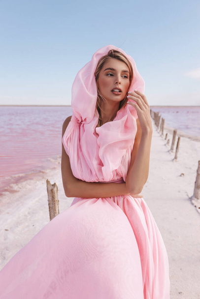 fashion outdoor photo of beautiful woman with blond hair in luxurious dress posing in pink salt lake - Photo, image