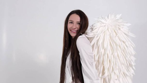 Ritratto di una donna sorridente a immagine di un angelo mostra le mani un cuore. Ragazza con lunghi capelli lisci su uno sfondo bianco. Concetto di San Valentino. Rallentatore - Foto, immagini