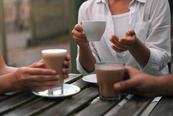 Friends drinking coffee and cocoa at wooden table in outdoor cafe, closeup - Fotografie, Obrázek