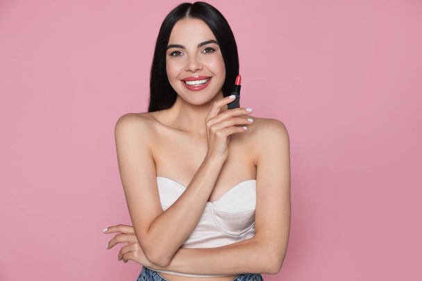 Young woman with beautiful makeup holding glossy lipstick on pink background - Zdjęcie, obraz