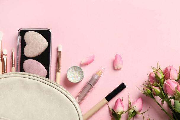 Set of makeup products with bag and roses on light pink background, flat lay. Space for text - Foto, afbeelding