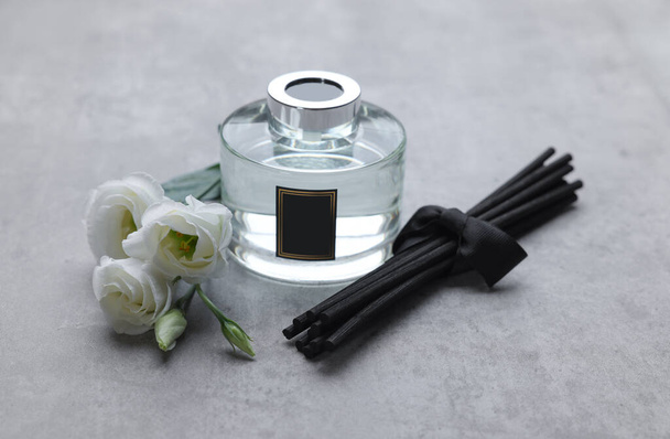 Reed sticks, glass bottle with aromatic liquid and eustoma flowers on gray marble table - Foto, afbeelding