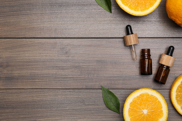 Bottles of essential oil with orange slices and leaves on wooden table, flat lay. Space for text - Foto, Imagem