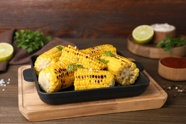 Tasty grilled corn and ingredients on wooden table - Фото, изображение