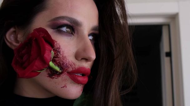 Makeup for Halloween, rose flower in mouth. Portrait of a girl holding a red rose in her mouth. High quality 4k video - Valokuva, kuva