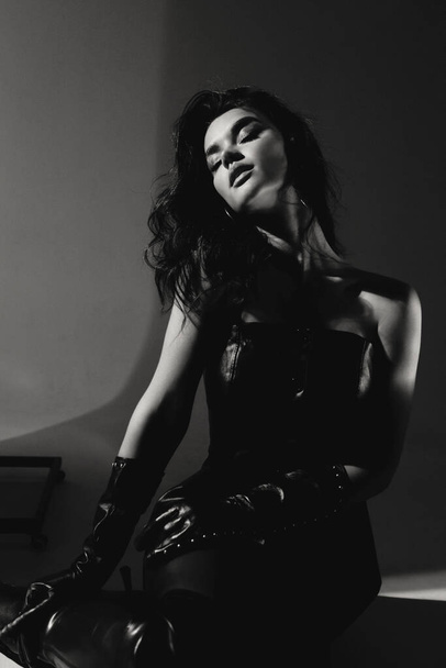 fashion photo of beautiful woman with dark hair in elegant outfit and leather gloves posing in studio - Photo, image