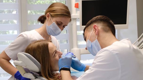 Nello studio dentistico. Un medico e un assistente curano i denti di una giovane donna. Trattamento tempestivo dei denti. Malattie della cavità orale - Foto, immagini