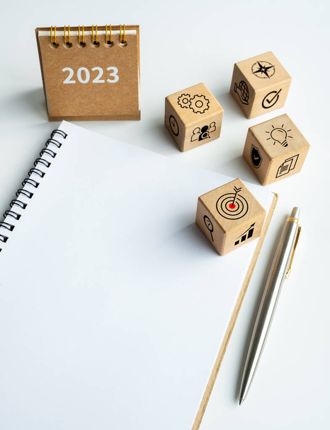 Proces biznesowy i plan na sukces ikony drewniane bloki sześcianu z 2023 mały rok kalendarzowy biurko na pusty notatnik z piórem na białym tle z miejsca do kopiowania, w stylu pionowym. Szczęśliwego Nowego Roku 2023. - Zdjęcie, obraz