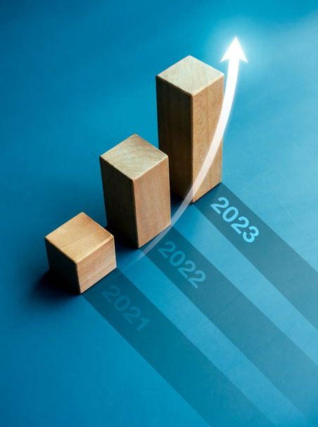 Brillante subida de flecha en bloques de cubo de madera, gráfico de barras pasos sobre fondo azul con números de año, 2023, 2022, 2021, estilo vertical. Crecimiento y desarrollo empresarial a los conceptos de éxito. - Foto, imagen