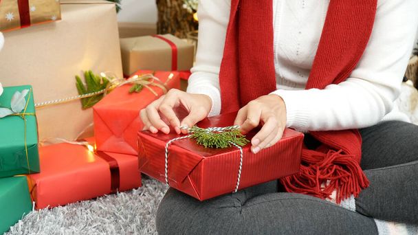 居心地の良いリビングルームでプレゼントをラップ女性の手を閉じます。クリスマスギフトボックスをクリスマスツリーの下に包んでいる女性。アジアの女性の装飾バブルボールクリスマスツリーでクリスマス休暇冬の季節のお祝い - 写真・画像