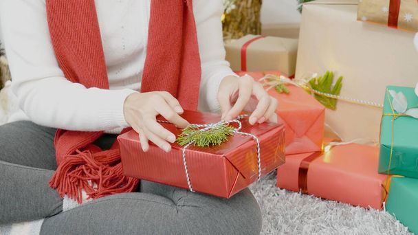 Close up woman hands wrap present gift in cozy living room. Woman wrapping christmas gift box under xmas tree. Asian woman decor bauble ball christmas tree in xmas holiday winter seasonal celebration - Foto, immagini