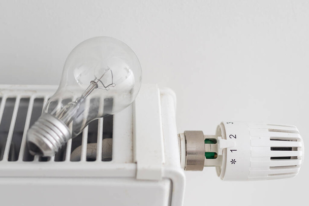 Heizung, Energiekrise und Verbrauchskonzept - Glühbirne am Heizkörper zu Hause - Foto, Bild