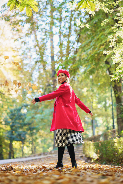 Koko vartalon puolella näkymä positiivinen nainen punaisissa vaatteissa pyörii ympäri seistessään kujalla kuivattuja lehtiä syksyllä puistossa - Valokuva, kuva